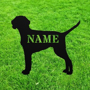 May include: Black metal silhouette of a dog standing on a green lawn. The dog's silhouette has the word "NAME" cut out of it.