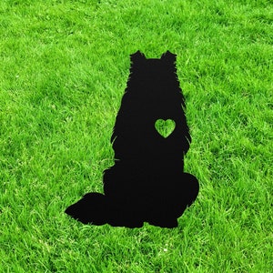 May include: Black metal silhouette of a dog sitting with a heart cutout in its chest. The silhouette is on a green grassy background.