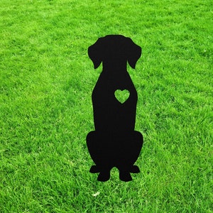 May include: A solid black silhouette of a sitting dog with floppy ears and a heart-shaped cutout located on the chest area. The figure is rendered in a flat, two-dimensional style with a smooth outline, depicting the animal in a seated position.
