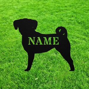 May include: Black metal silhouette of a dog, standing on green grass. The word "NAME" is cut out of the dog's body. The dog has a curled tail and floppy ears. The background is a field of green grass.