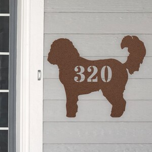May include: A brown dog silhouette with the house number 320 printed on it. The silhouette is made of a textured material and is mounted on a light gray wooden surface.