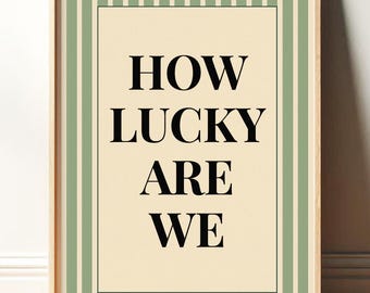 May include: A framed art print with the words "HOW LUCKY ARE WE" in bold black letters. The background is a light beige color, framed by a black border. The outer border features vertical stripes of light green and white, all within a wooden frame.
