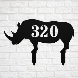 May include: Black metal silhouette of a rhinoceros with the number 320 cut out of the body. The rhino is standing on two stakes, which can be used to place the silhouette in the ground.
