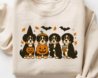 May include: A cream-colored sweatshirt featuring a Halloween-themed graphic. The graphic depicts four Bernese Mountain Dogs dressed in Halloween costumes, including a witch hat, pumpkin, and vampire cape. Bats and fall leaves are also included.