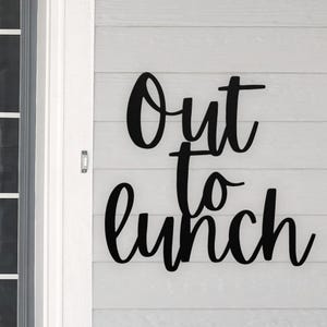 May include: Black metal sign with the words "Out to Lunch" in a cursive font.