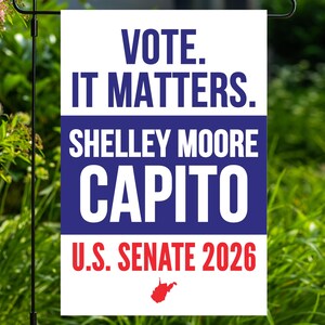 May include: A rectangular garden flag featuring the text VOTE. IT MATTERS. in blue, SHELLEY MOORE CAPITO in white on a blue background, and U.S. SENATE 2026 in red. A small red silhouette of the state of West Virginia is centered at the bottom.