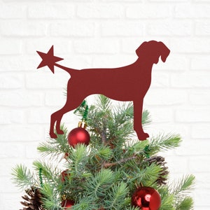 May include: Red metal dog silhouette Christmas tree topper with a star on its tail, sitting on a green pine tree with red ornaments.