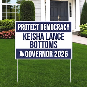 May include: A rectangular political yard sign with a white background and dark blue horizontal bands. The text reads PROTECT DEMOCRACY, KEISHA LANCE BOTTOMS, and GOVERNOR 2026, accompanied by a white silhouette of the state of Georgia on the sign.