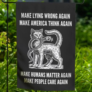 May include: Black and white garden flag with a cat holding a snake in its mouth. The flag has the text "Make Lying Wrong Again", "Make America Think Again", "Make Humans Matter Again", and "Make People Care Again".