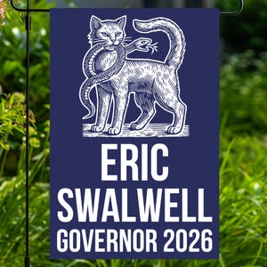 May include: A navy blue garden flag features a white illustration of a cat holding a snake. The flag includes the text "ERIC SWALWELL GOVERNOR 2026" in white block letters. The flag is displayed outdoors with green foliage in the background.