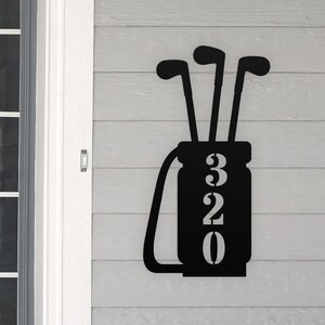 May include: Black metal golf bag house number sign with the number 320. The sign is shaped like a golf bag with three golf clubs sticking out of the top.