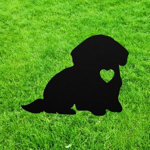 May include: Black silhouette of a dog sitting on a green grassy lawn. The dog has a heart cut out of its chest.