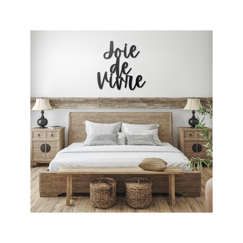 Puede incluir: Una cama con estructura de madera con un edred&oacute;n y almohadas blancas. La cabecera est&aacute; hecha de madera y tiene un aspecto r&uacute;stico. Hay un banco de madera delante de la cama con dos cestas de mimbre. La pared detr&aacute;s de la cama tiene un letrero de metal negro que dice "Joie de vivre".