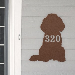 May include: A brown metal silhouette of a dog sitting with its tail curled around its legs. The number 320 is cut out of the dog's body in white.