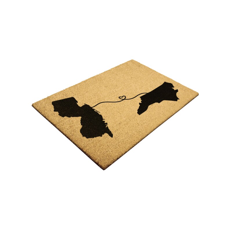 May include: A brown coir doormat with the outlines of the states of Maryland and North Carolina in black. A black line connects the two states, forming a heart shape in the middle.