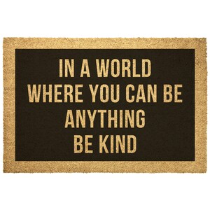 May include: A brown doormat with the text "In a world where you can be anything be kind" in gold lettering.