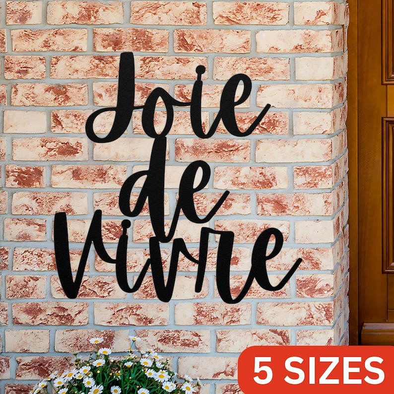 Puede incluir: Decoraci&oacute;n de pared de metal negro con la frase francesa "Joie de Vivre" en una fuente cursiva. La decoraci&oacute;n est&aacute; montada en una pared de ladrillo. El texto "5 TAMA&Ntilde;OS" es visible en la esquina inferior derecha de la imagen.