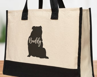 May include: A beige canvas tote bag with black accents and handles. A black silhouette of a dog is printed on the front, with the name "Buddy" in cursive script. The bottom of the bag is black.