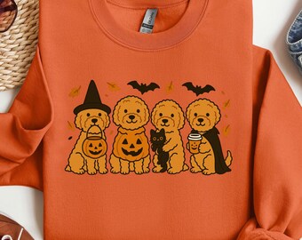 May include: Orange sweatshirt featuring a Halloween-themed graphic. The design includes four cartoon dogs dressed in costumes, including a witch hat, pumpkin, and cape. Bats and autumn leaves are also part of the design.