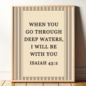 May include: Framed print with the text "WHEN YOU GO THROUGH DEEP WATERS, I WILL BE WITH YOU ISAIAH 43:2". The print has a cream-colored background with black text, framed by a beige and white striped border and a wooden frame.