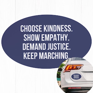 May include: A blue oval sticker with the text "CHOOSE KINDNESS. SHOW EMPATHY. DEMAND JUSTICE. KEEP MARCHING."  The sticker is on the back of a white car.