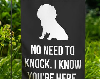 May include: Black garden flag with a white silhouette of a dog sitting down. The text "NO NEED TO KNOCK. I KNOW YOU'RE HERE." is printed in white below the dog.