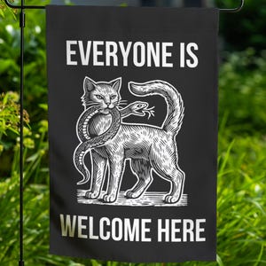 May include: Black garden flag with a white illustration of a cat with a snake wrapped around its body. The text "Everyone is Welcome Here" is printed in white below the image.