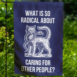 May include: A blue garden flag with a white cat illustration holding a snake in its mouth. The text on the flag reads "What is so radical about caring for other people?"