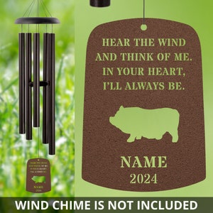 May include: A brown and green memorial plaque with a pig silhouette, the text "Hear the wind and think of me. In your heart, I'll always be." and a space for a name and year. The text "Wind chime is not included" is at the bottom of the image.
