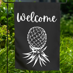 May include: Black welcome garden flag with a white pineapple design. The pineapple is stylized with a detailed outline of the fruit and leaves.