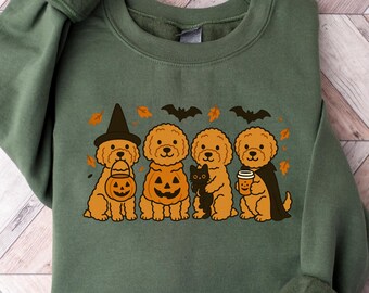 May include: Green sweatshirt featuring a Halloween-themed graphic. The design includes four cartoon dogs dressed in costumes, including a witch hat, pumpkin, and cape. A black cat and fall leaves are also included in the design.