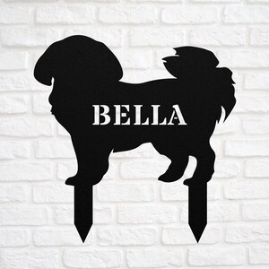 May include: Black metal silhouette of a dog with the name "BELLA" written on it. The silhouette is attached to two metal stakes for planting in the ground.