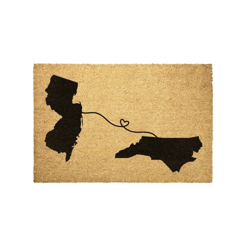 May include: A brown coir doormat with the outlines of New Jersey and North Carolina in black. A black line with a heart shape connects the two states.