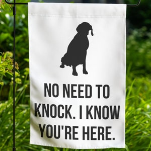 May include: White garden flag with a black silhouette of a dog sitting. The text "NO NEED TO KNOCK. I KNOW YOU'RE HERE." is printed below the dog.