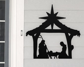 May include: Black metal silhouette of a nativity scene with Mary, Joseph, and the baby Jesus in a manger. A star is above the manger.