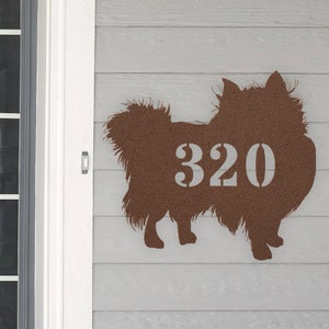 May include: A brown metal silhouette of a dog with the house number 320 cut out of the dog's body. The silhouette is mounted on a light gray wooden surface.