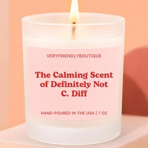 May include: A lit, white candle in a frosted glass jar. The label reads "The Calming Scent of Definitely Not C. Diff" in red text. The text "VERYFRIENDLYBOUTIQUE" is above the main text. The candle is hand-poured in the USA.