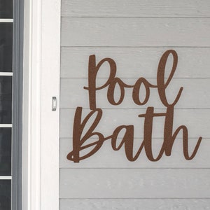 May include: A brown metal sign with the words "Pool Bath" in a cursive font.