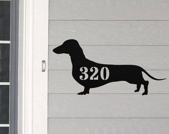 May include: Black metal silhouette of a dachshund with the house number 320 cut out of the body. The silhouette is mounted on a light gray wooden surface.