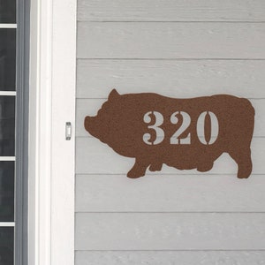 May include: A brown metal pig silhouette with the number 320 cut out of the center. The pig is mounted on a light gray wooden surface.