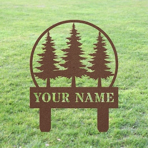 May include: A brown metal yard sign with a circle design featuring three pine trees. The sign has a rectangular space at the bottom with the text "YOUR NAME" in white.
