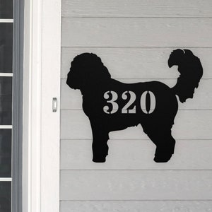 May include: Black metal silhouette of a dog with the house number 320 displayed on its side. The silhouette is mounted on a light gray wooden surface.
