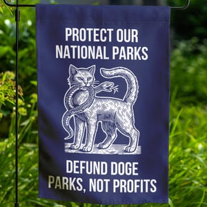 May include: A blue garden flag with a white illustration of a cat holding a snake in its mouth. The text "PROTECT OUR NATIONAL PARKS" is at the top of the flag and "DEFUND DOGE PARKS, NOT PROFITS" is at the bottom.