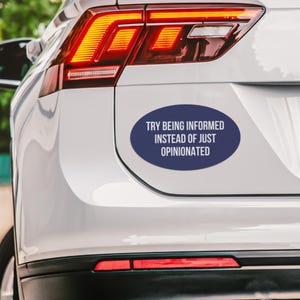 May include: Oval-shaped navy blue bumper sticker with white text that reads "TRY BEING INFORMED INSTEAD OF JUST OPINIONATED." The sticker is affixed to the rear of a white car, near the taillight.