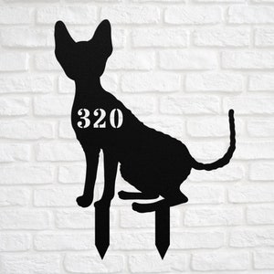 May include: Black metal silhouette of a cat with the number 320 on its side. The cat is sitting on two metal stakes, which are used to insert the silhouette into the ground.