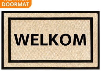 May include: Rectangular doormat with the word "WELKOM" in bold black letters on a beige background. The mat has a black border and the words "ALL WEATHER DOORMAT" in an orange box in the upper left corner.