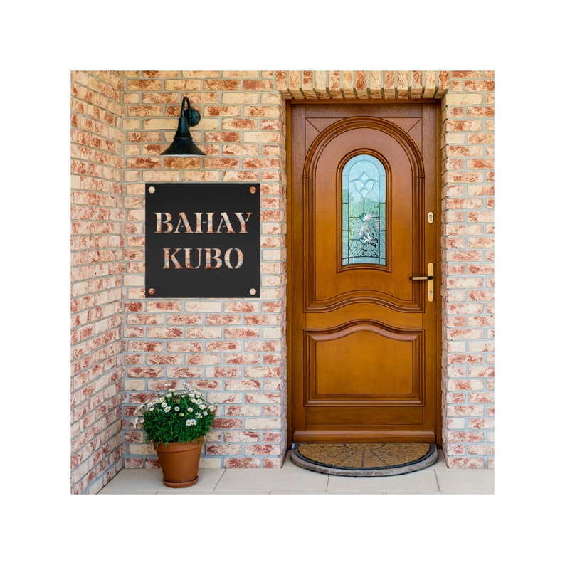 May include: A black metal sign with the words "BAHAY KUBO" in white lettering. The sign is mounted on a brick wall next to a wooden door with a glass window.