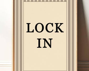 May include: A framed print with the words "LOCK IN" in bold black letters on a cream-colored background. The frame is light wood, and the print has a striped border in shades of beige and gray.