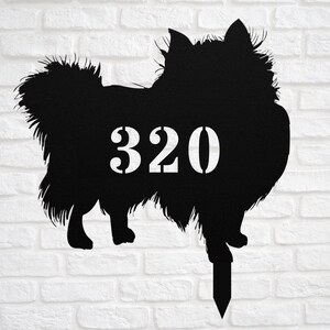 May include: Black metal yard sign in the shape of a dog, with the number 320 in white. The dog silhouette has a fluffy appearance and is mounted on a stake for easy placement in a garden or yard.