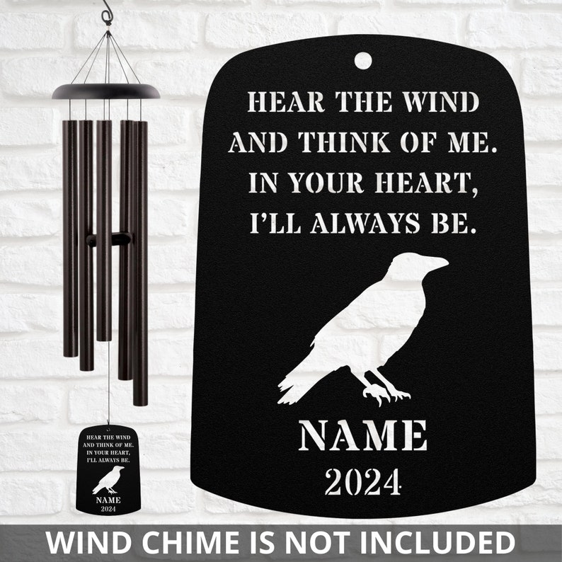May include: Black metal wind chime hanger with a white raven silhouette and the text "Hear the wind and think of me. In your heart, I'll always be."  The hanger also includes a space for a name and year.  "NAME 2024" is shown as an example.  "Wind chime is not included" is printed below the hanger.